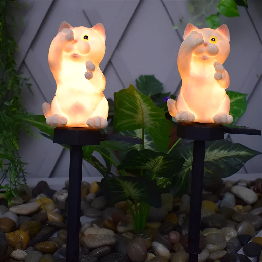 Brown resin cat-shaped solar garden light illuminating in a evening garden setting.