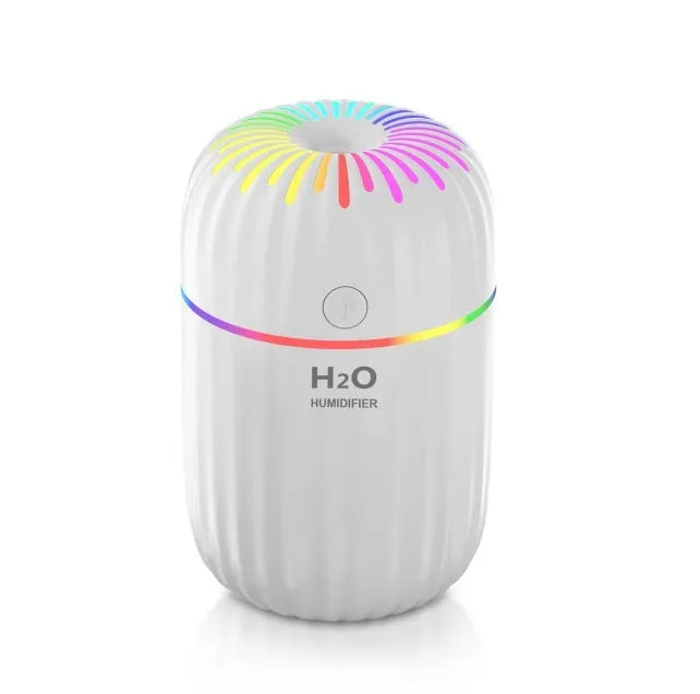 Small white USB humidifier with water tank on a wooden desk next to a laptop.