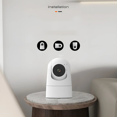 White indoor security camera with wide-angle lens on a table, showing power cable and mounting bracket.