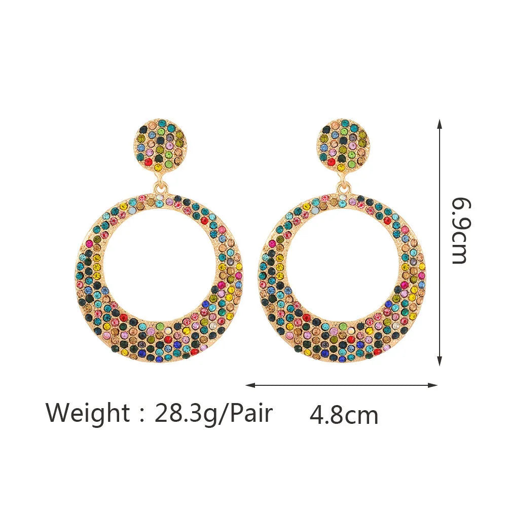 A pair of large round pendant drop earrings with colourful diamond details and a cartoon style on a metal alloy setting.