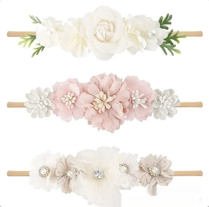 Three cloth flower-shaped hair bands for children in different styles on a light background