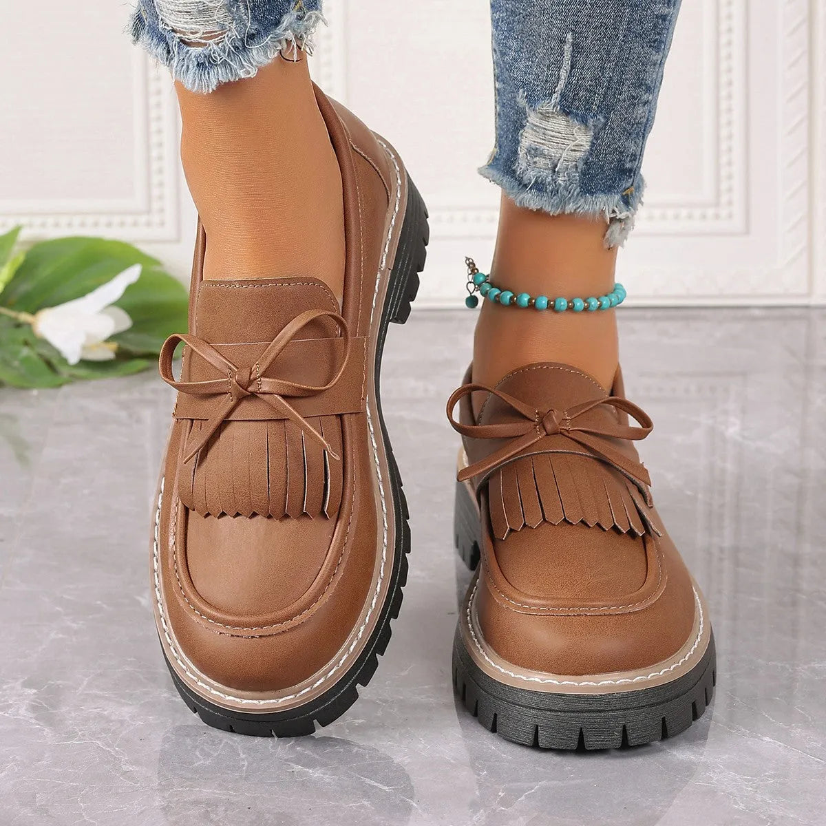 A pair of black plus size women's loafers with a tassel and bowknot decoration on a chunky rubber sole.