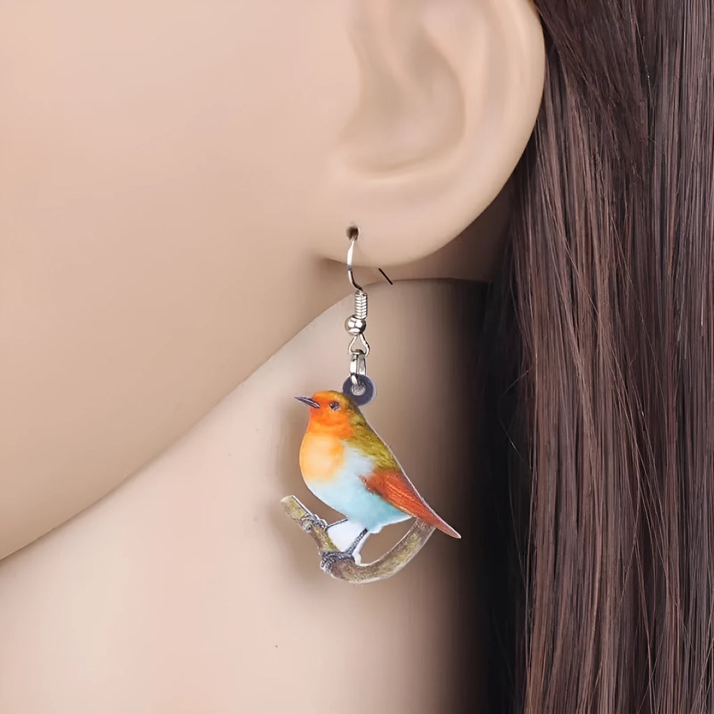 A pair of blue, white, and black acrylic drop earrings featuring a detailed Blue Tit bird and geometric snake patterns on a white background.