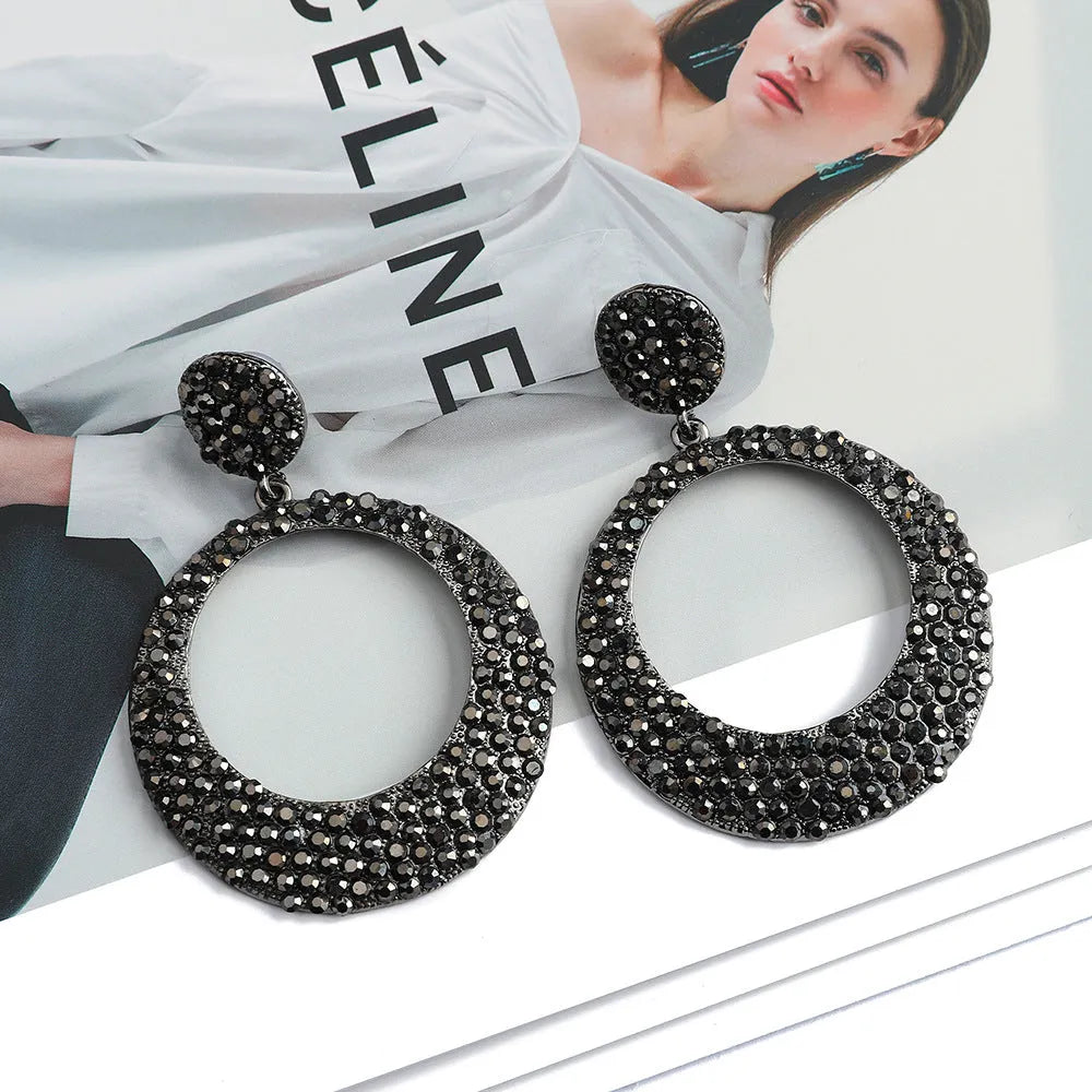 A pair of large round pendant drop earrings with colourful diamond details and a cartoon style on a metal alloy setting.