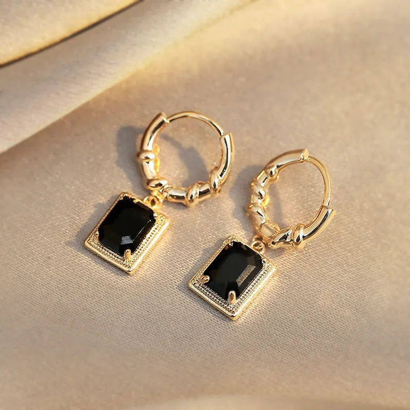 A pair of black geometric quadrilateral earrings with zircon stones on copper settings, shown against a plain background.