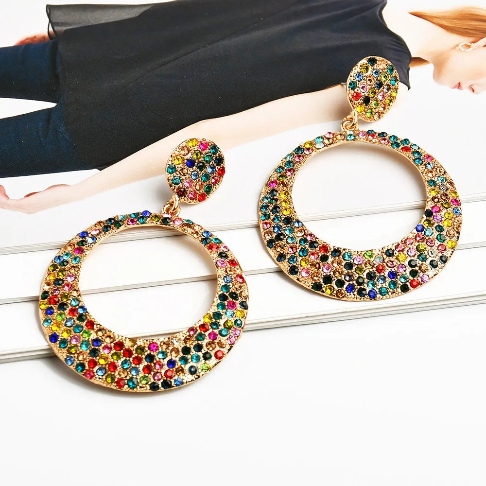A pair of large round pendant drop earrings with colourful diamond details and a cartoon style on a metal alloy setting.