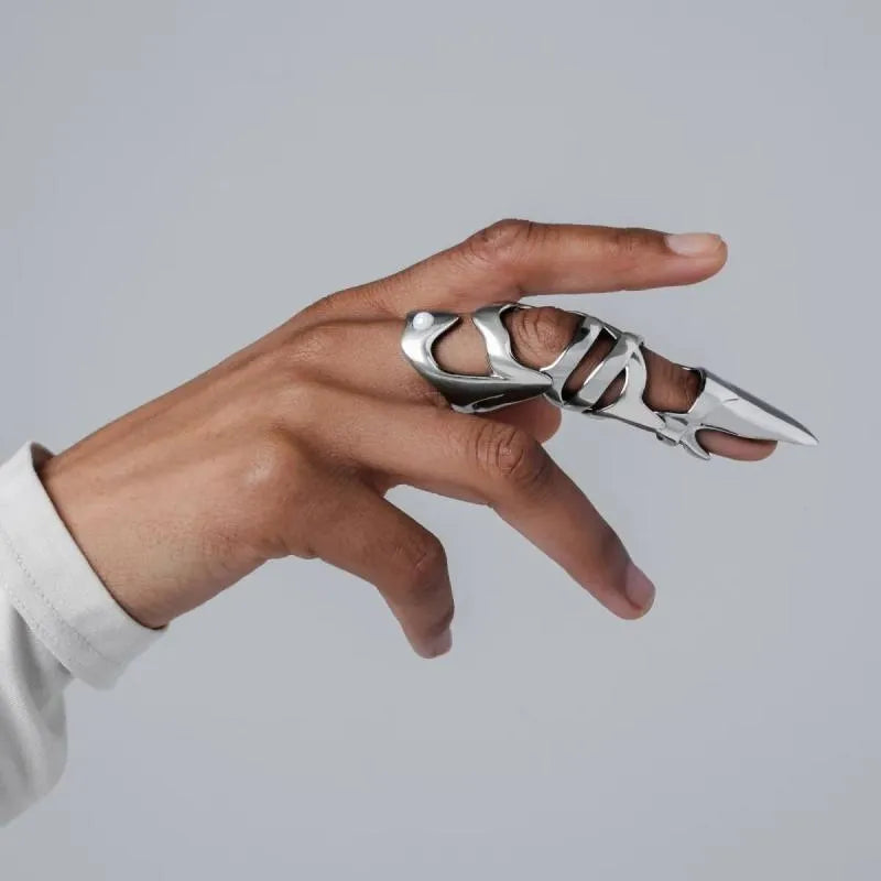 Silver-coloured metal finger cover with punk armour design shown on a model's finger.
