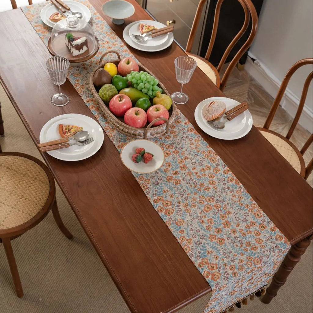Beige jacquard table runner with floral pattern and long tassels draped over a wooden wedding table.