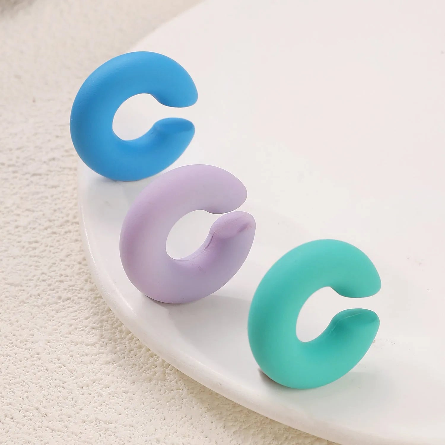 Round C-shaped clip-on earring with a matte coarse surface in a selection of candy colours.