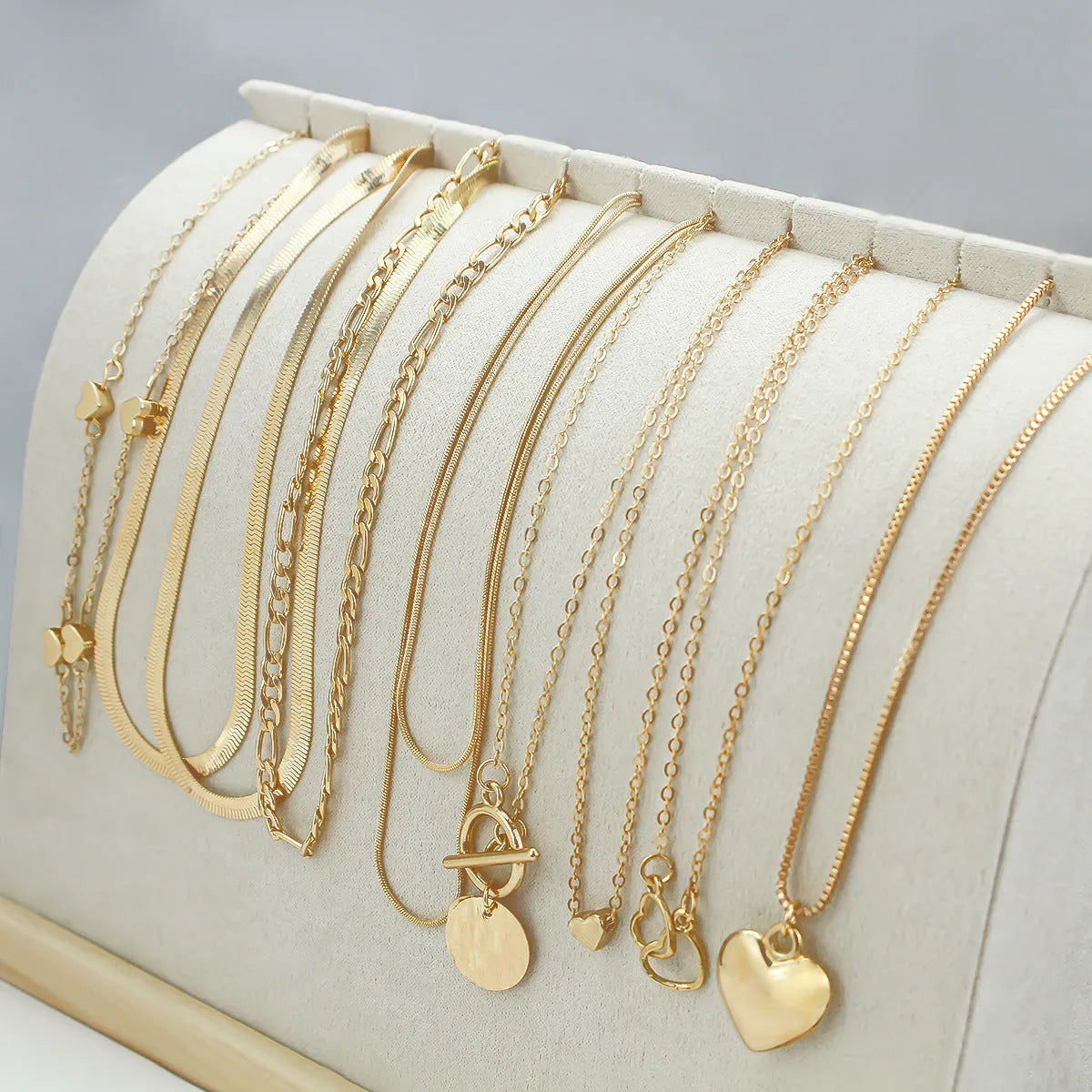 Set of ten gold-coloured women's necklaces with snake bone chains and alloy pendants on a white background.