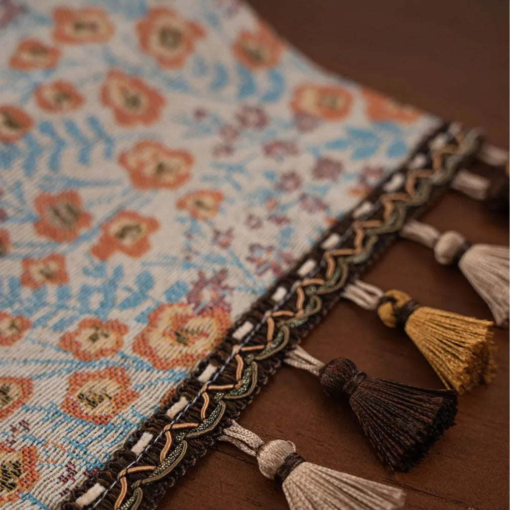 Beige jacquard table runner with floral pattern and long tassels draped over a wooden wedding table.