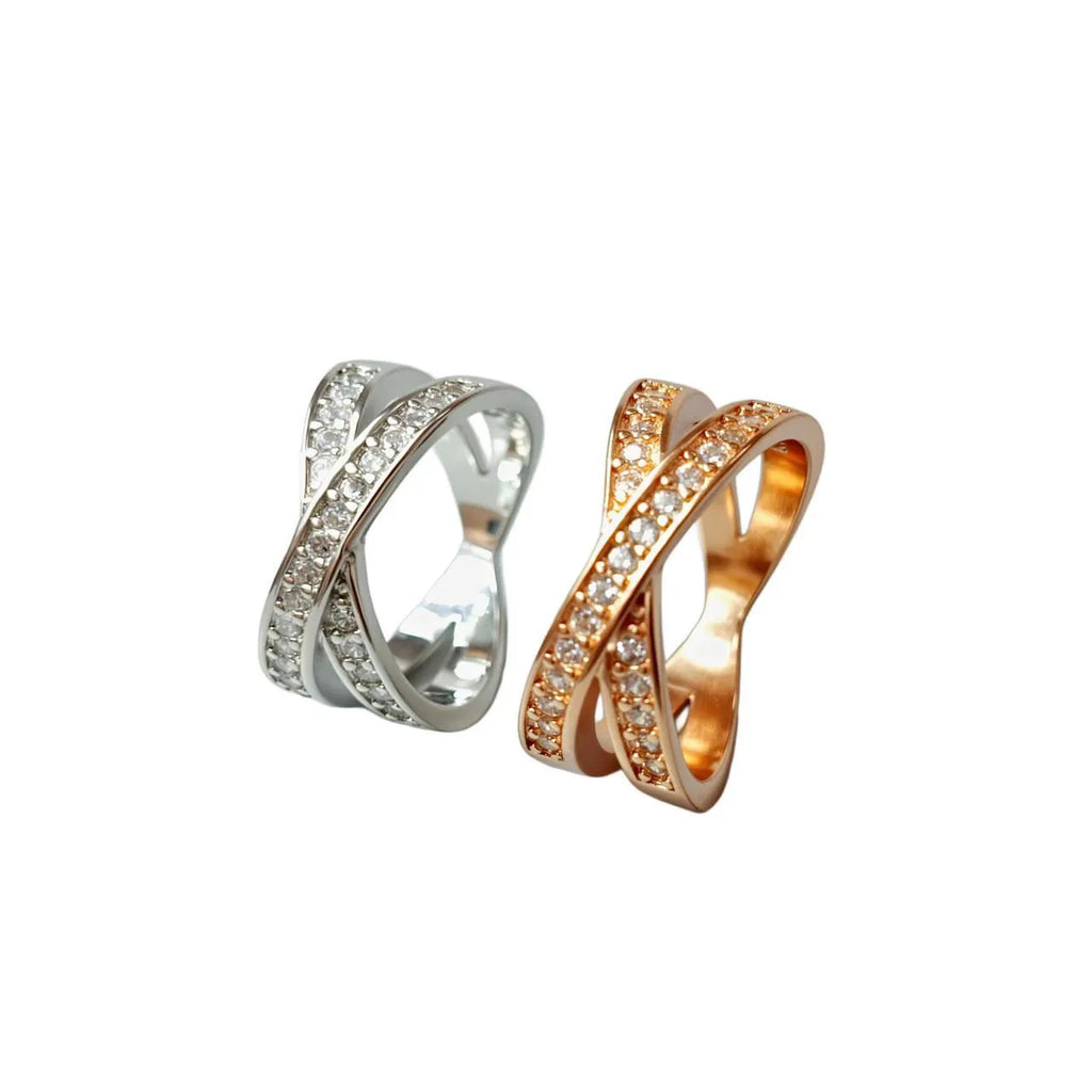 A geometric silver cross ring with small zircon stones on a person's hand, showing a simple band design.