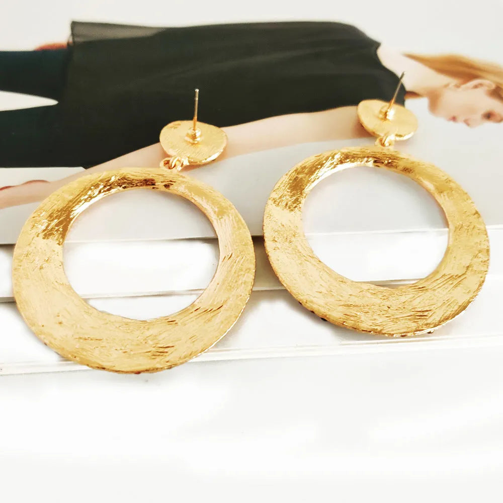 A pair of large round pendant drop earrings with colourful diamond details and a cartoon style on a metal alloy setting.