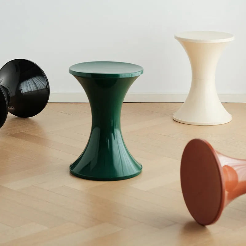A green plastic hourglass-shaped shoe changing stool on a wooden floor.
