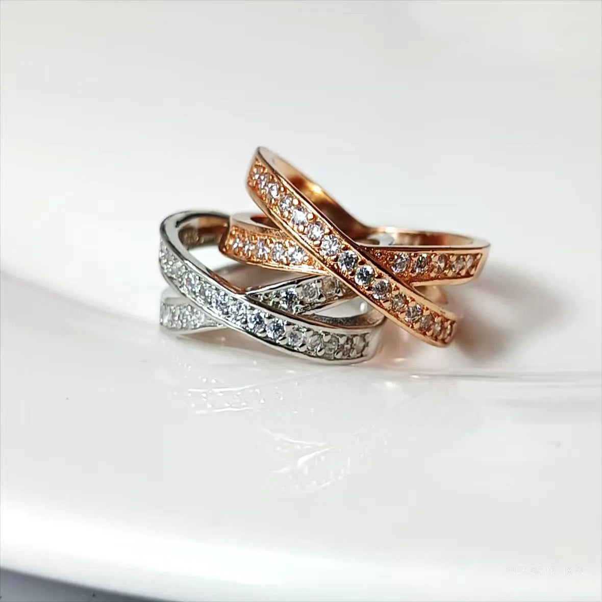 A geometric silver cross ring with small zircon stones on a person's hand, showing a simple band design.