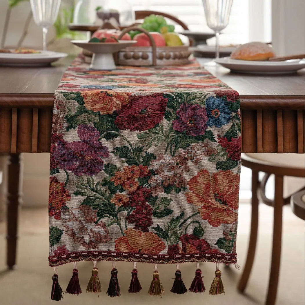 Beige jacquard table runner with floral pattern and long tassels draped over a wooden wedding table.