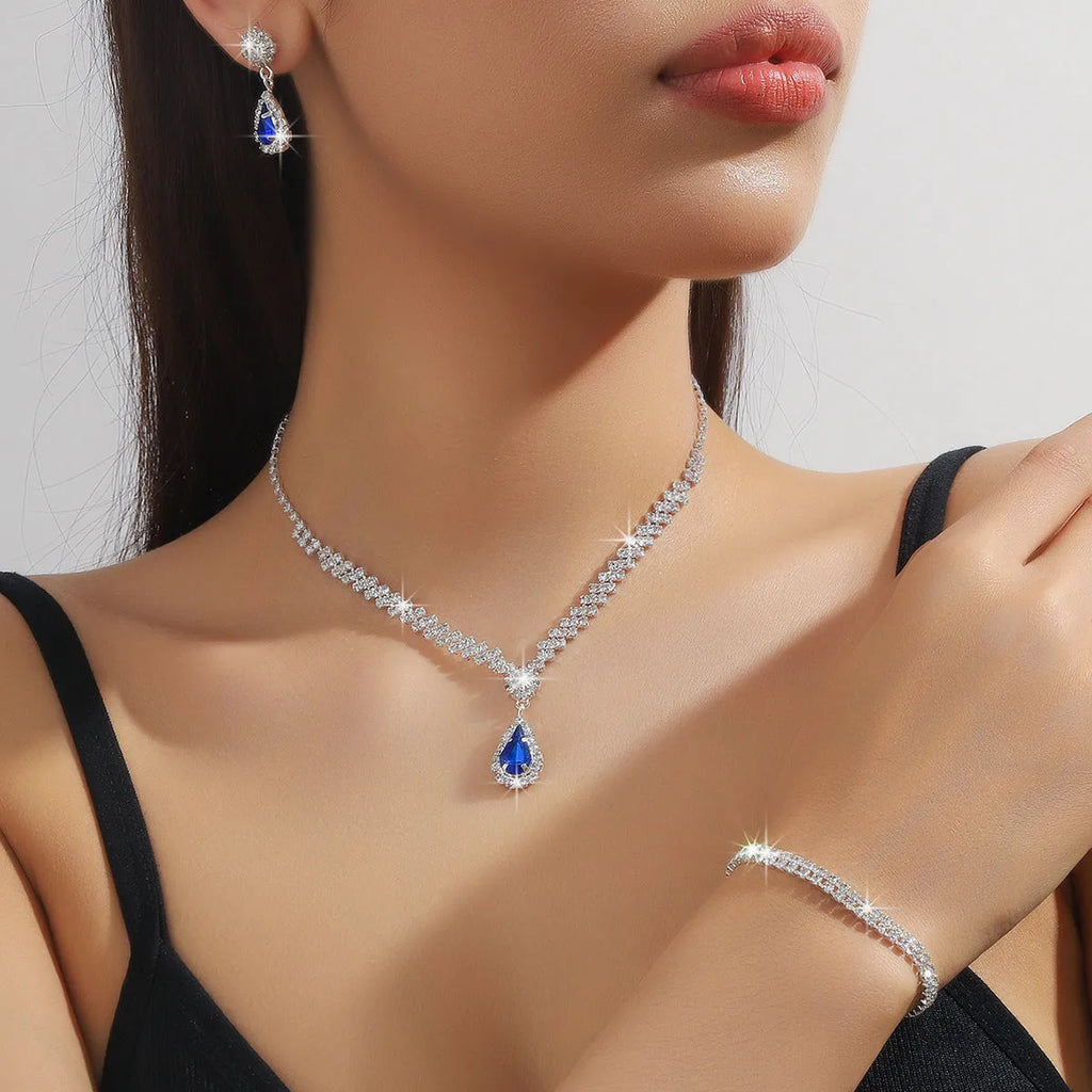 Women's blue claw chain necklace and drop rhinestone earrings set on white background.