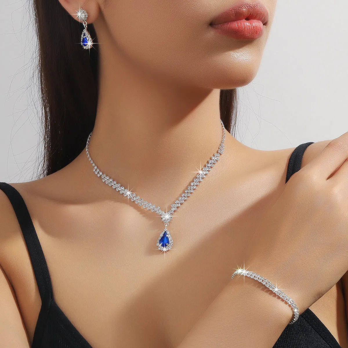 Women's blue claw chain necklace and drop rhinestone earrings set on white background.