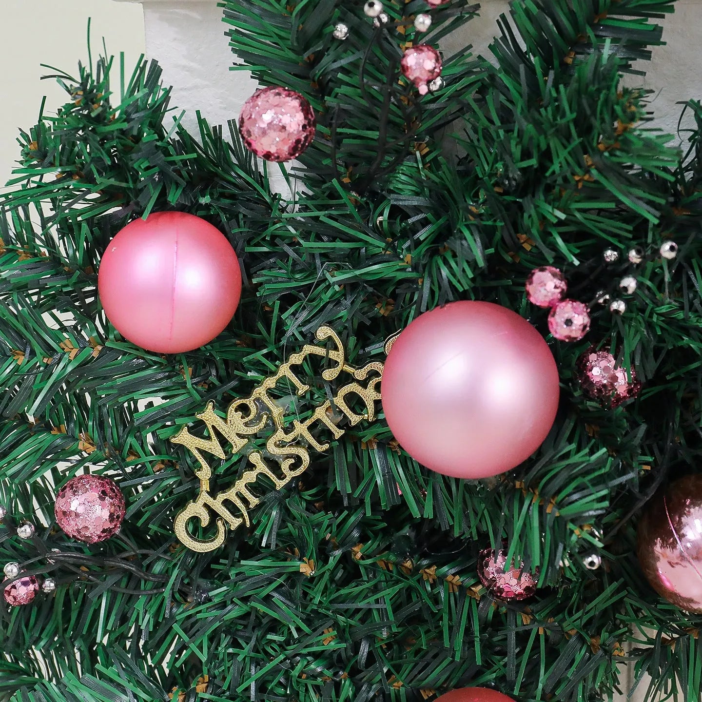 Pink artificial rattan Christmas garland with small fruit and LED lights draped over a banister
