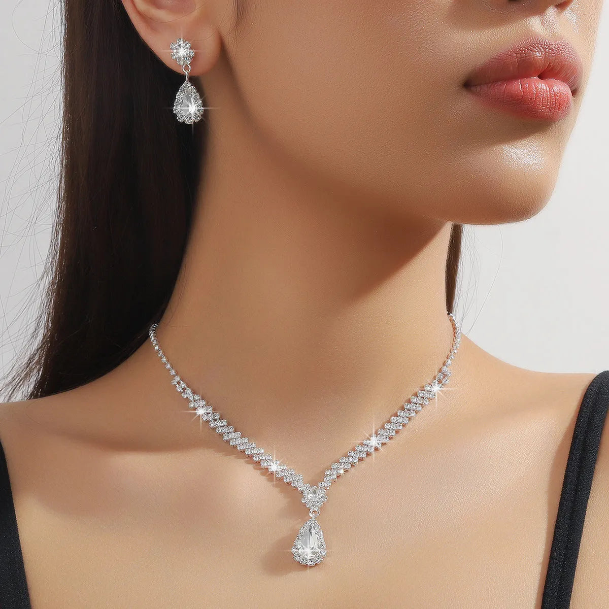 Women's blue claw chain necklace and drop rhinestone earrings set on white background.