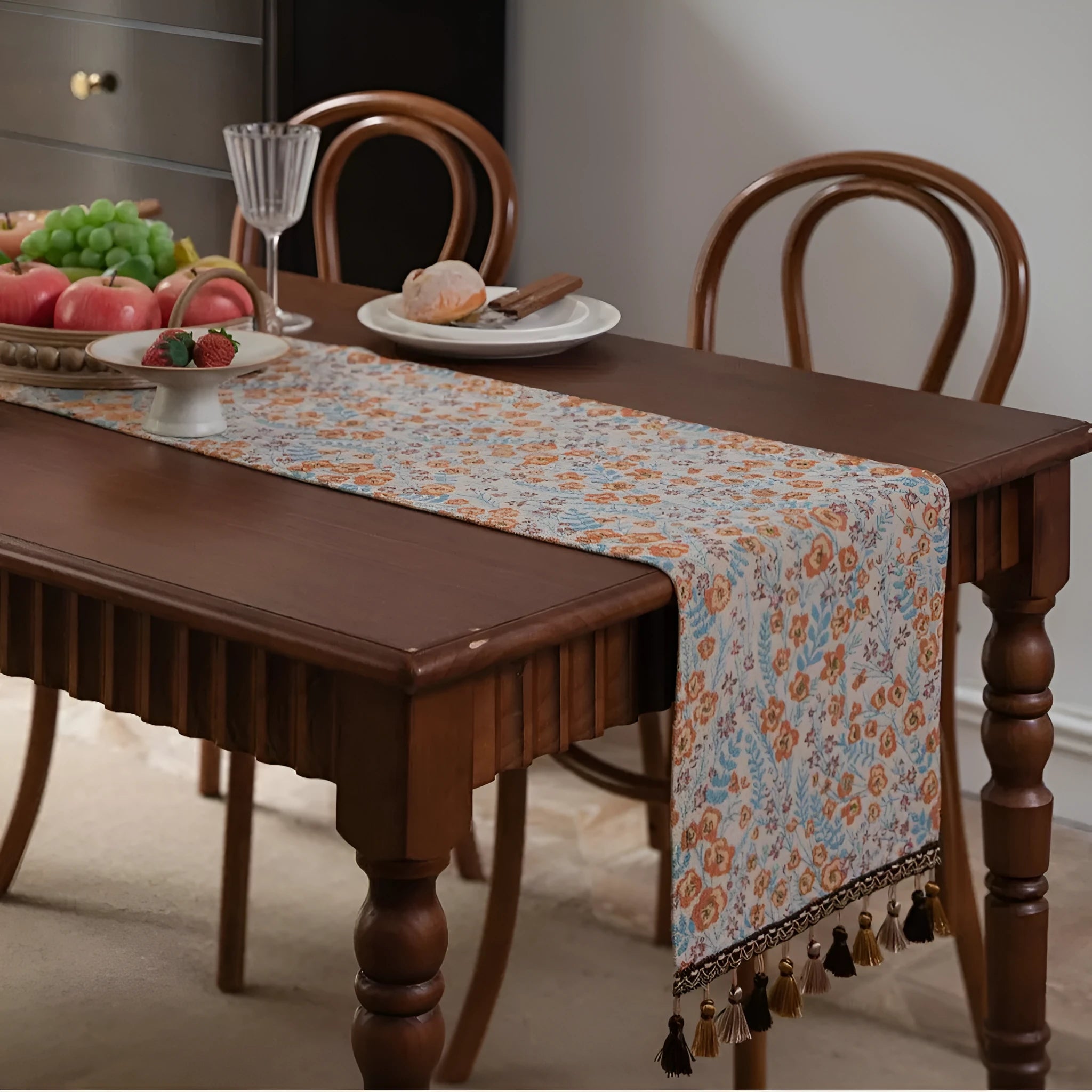 Beige jacquard table runner with floral pattern and long tassels draped over a wooden wedding table.