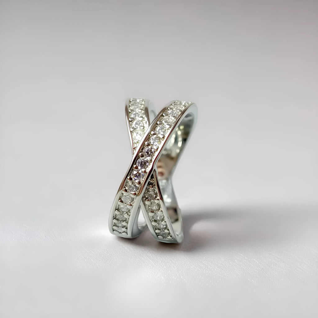 A geometric silver cross ring with small zircon stones on a person's hand, showing a simple band design.
