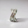 A geometric silver cross ring with small zircon stones on a person's hand, showing a simple band design.