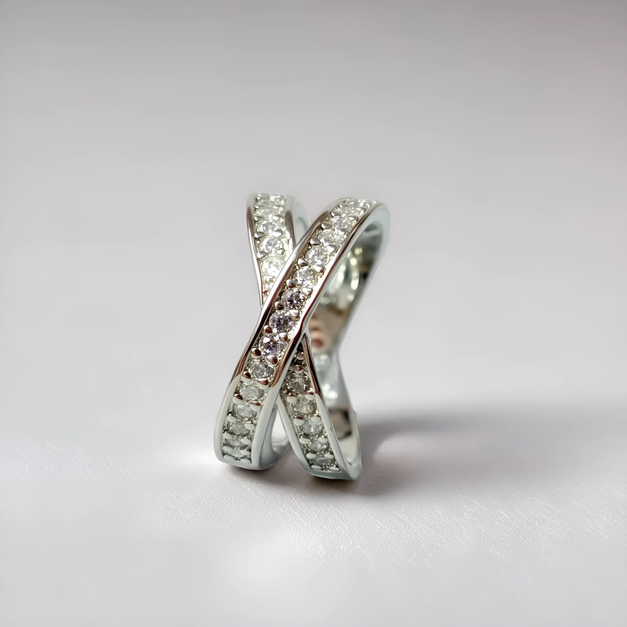 A geometric silver cross ring with small zircon stones on a person's hand, showing a simple band design.