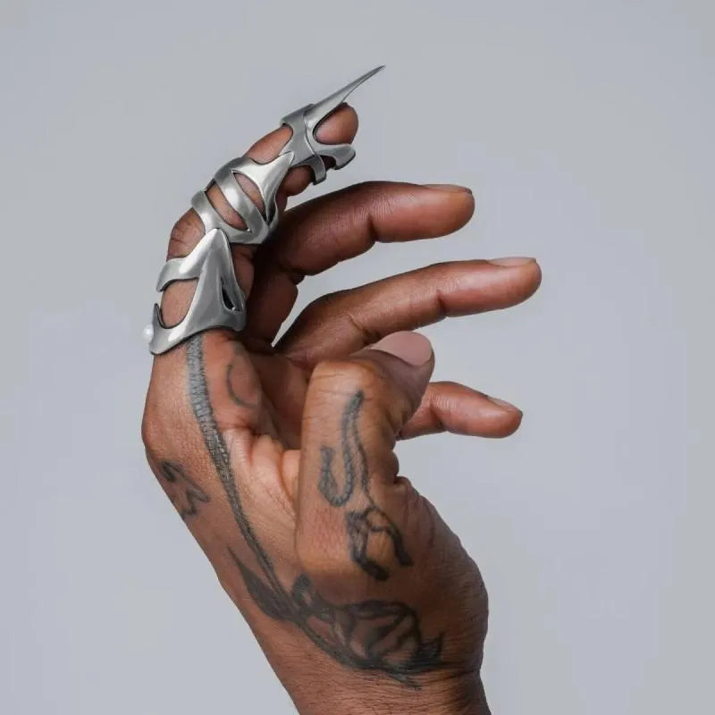 Silver-coloured metal finger cover with punk armour design shown on a model's finger.