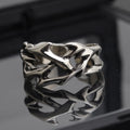 Copper geometric ring with thorn and flower design on a finger, showing adjustable opening.