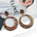 A pair of large round pendant drop earrings with colourful diamond details and a cartoon style on a metal alloy setting.