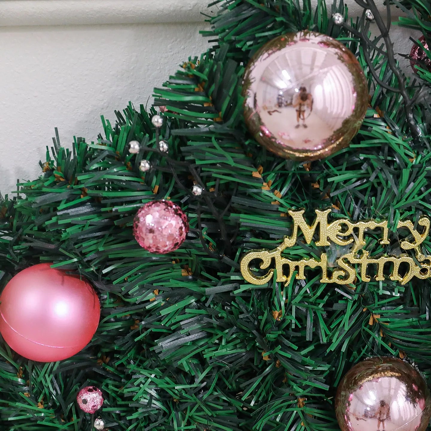 Pink artificial rattan Christmas garland with small fruit and LED lights draped over a banister