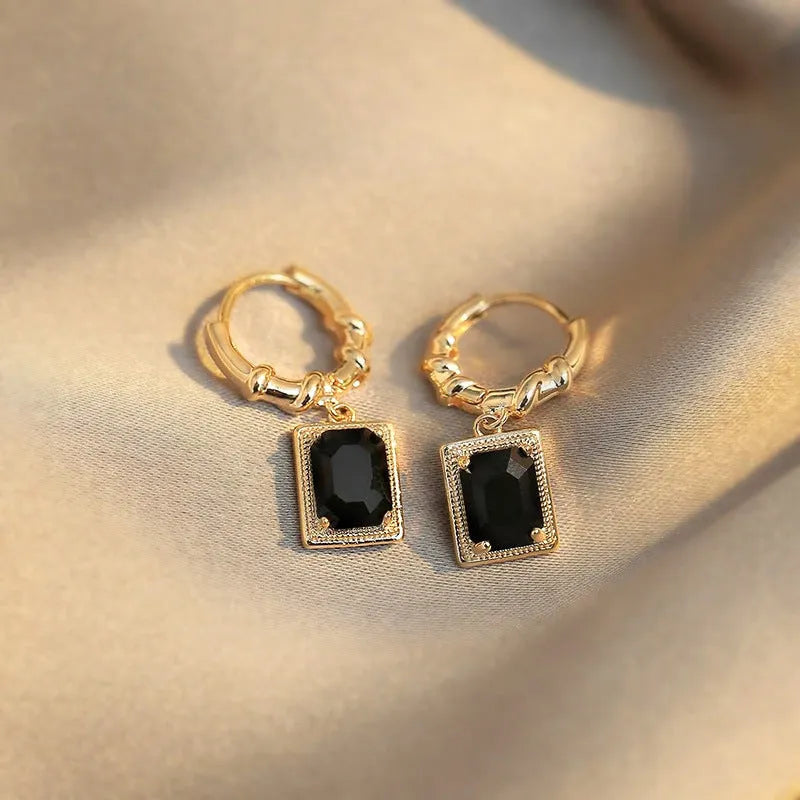 A pair of black geometric quadrilateral earrings with zircon stones on copper settings, shown against a plain background.