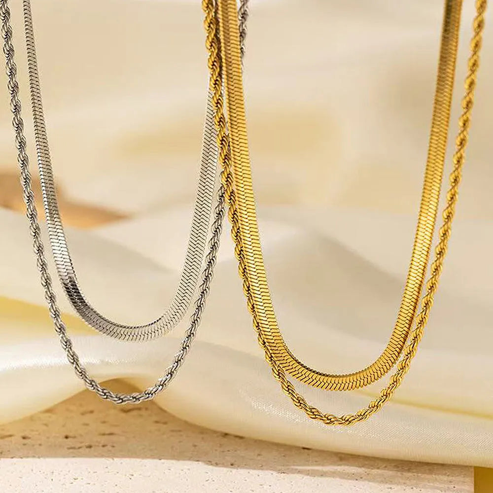 Women's silver geometric twist pendant necklace on adjustable snake bone chain against grey background.