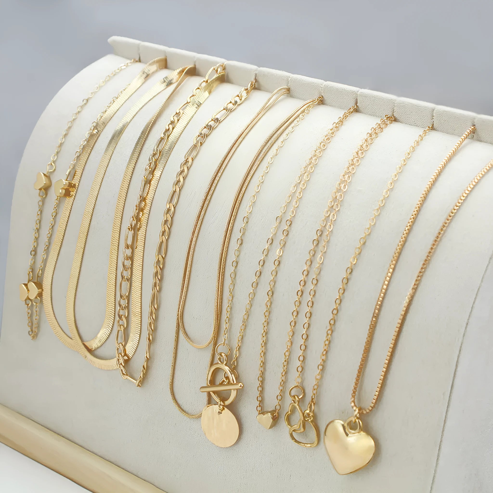 Set of ten gold-coloured women's necklaces with snake bone chains and alloy pendants on a white background.