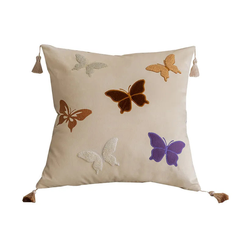Square beige cushion with butterfly embroidery on a sofa, showing purple and black colour options.
