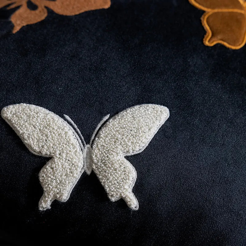 Square beige cushion with butterfly embroidery on a sofa, showing purple and black colour options.