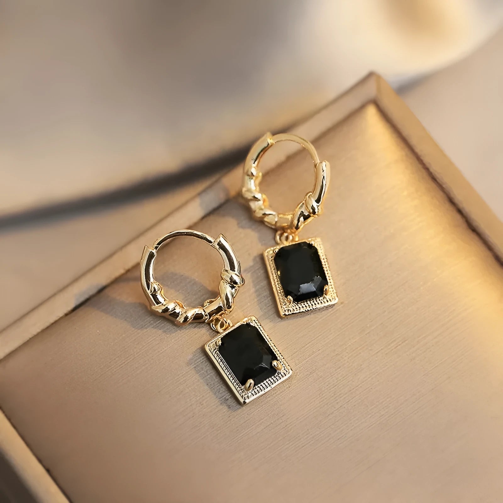 A pair of black geometric quadrilateral earrings with zircon stones on copper settings, shown against a plain background.