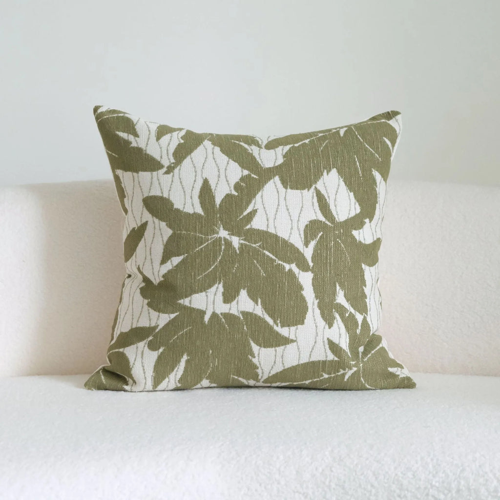 Green striped and botanical pattern decorative pillow with tassels on a bed.