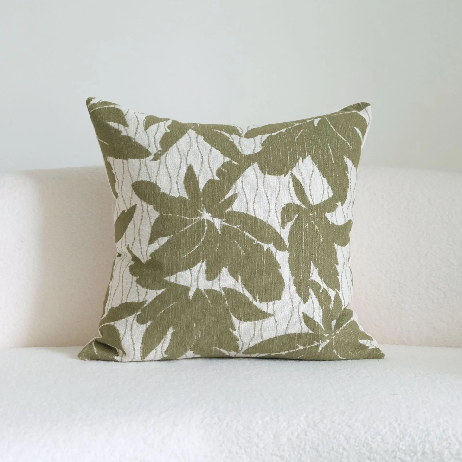 Green striped and botanical pattern decorative pillow with tassels on a bed.