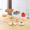White plastic cube-shaped dessert display stand with multiple tiers for cupcakes and pastries.
