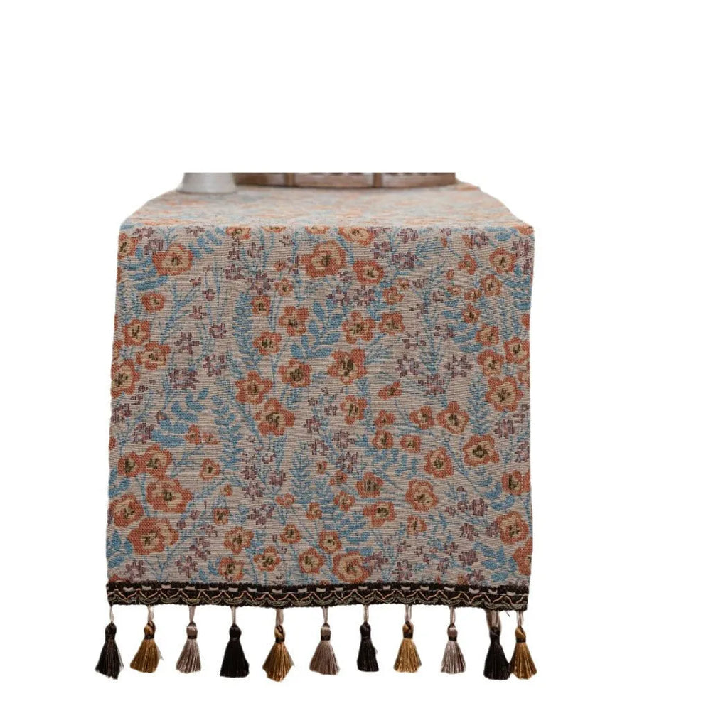 Beige jacquard table runner with floral pattern and long tassels draped over a wooden wedding table.