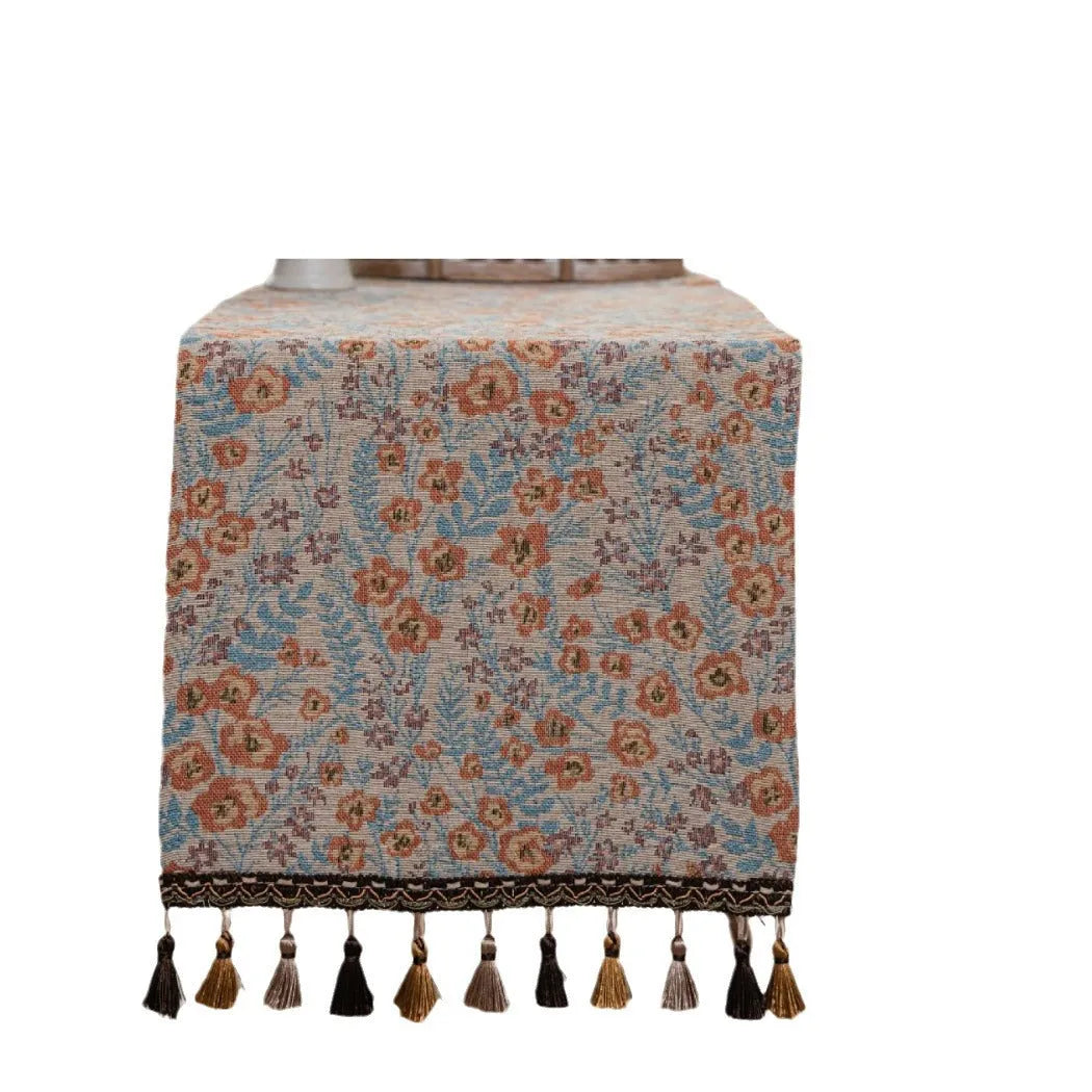Beige jacquard table runner with floral pattern and long tassels draped over a wooden wedding table.