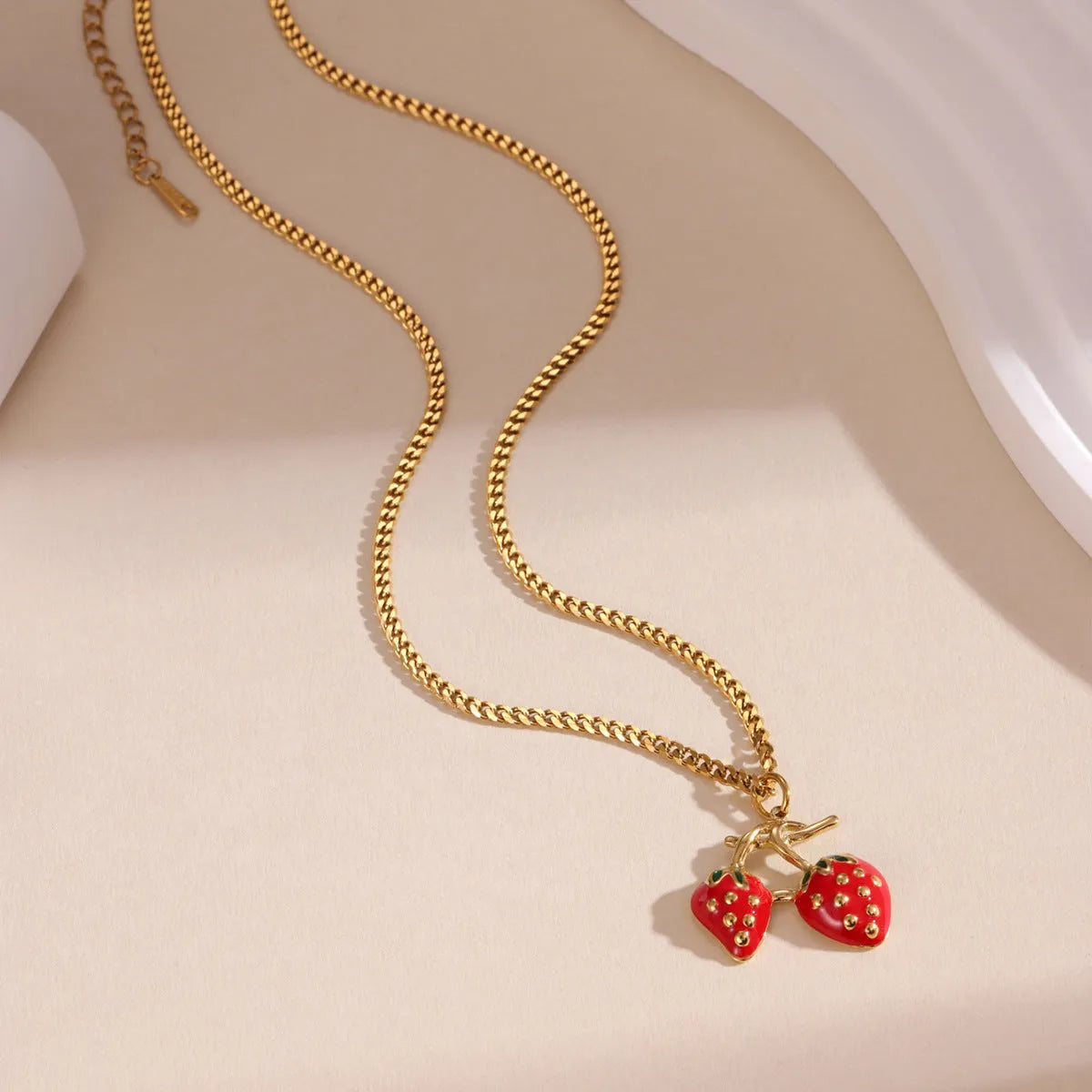 Close-up of a women's stainless steel necklace with a small red strawberry fruit pendant on a silver chain.