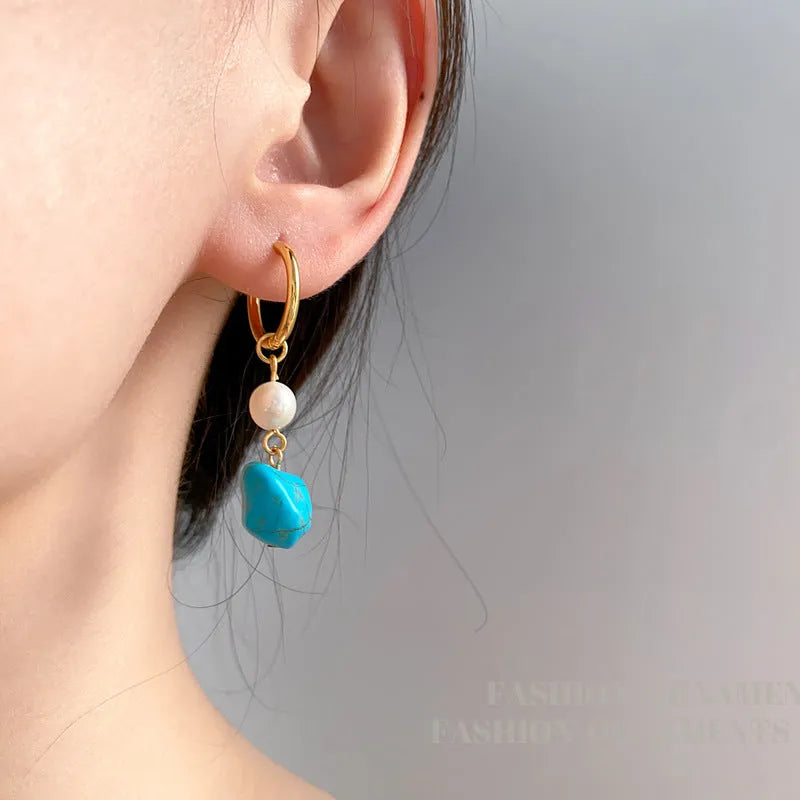 A pair of geometric copper earring clips with turquoise stones and cultured pearls, one short and one long.