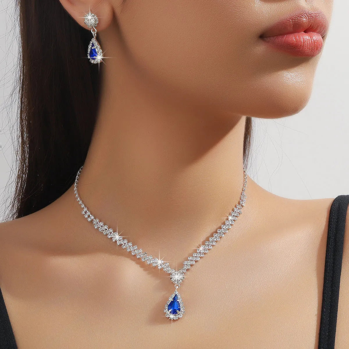 Women's blue claw chain necklace and drop rhinestone earrings set on white background.