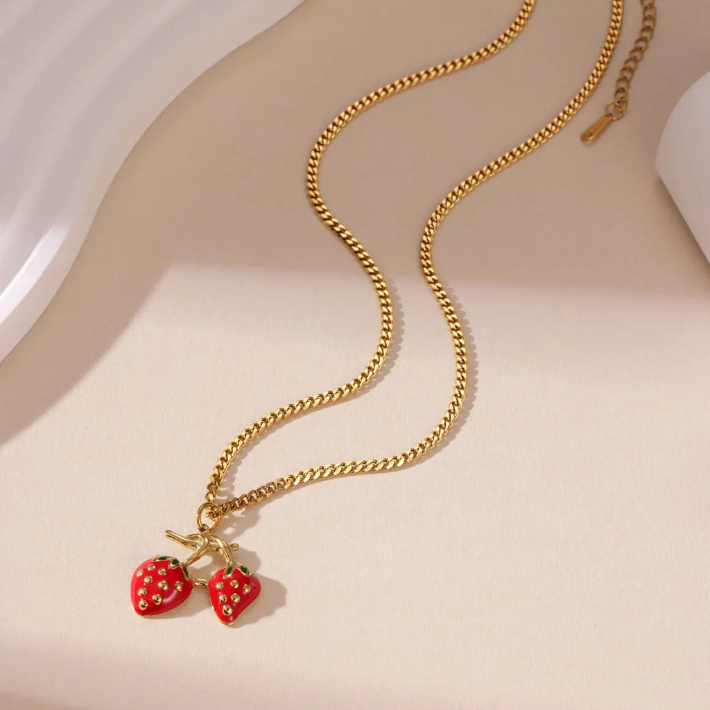 Close-up of a women's stainless steel necklace with a small red strawberry fruit pendant on a silver chain.
