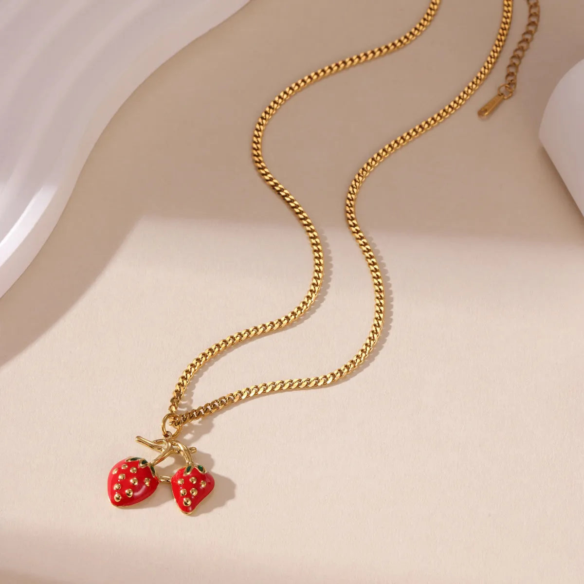 Close-up of a women's stainless steel necklace with a small red strawberry fruit pendant on a silver chain.