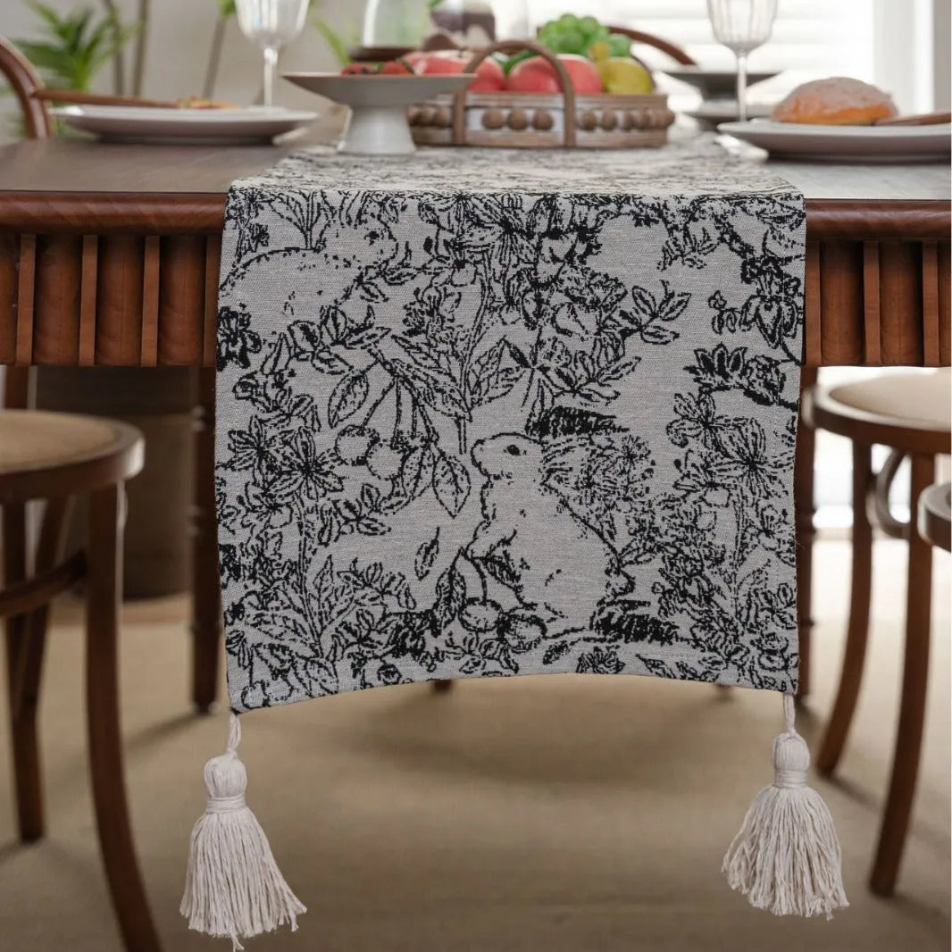 Beige jacquard table runner with floral pattern and long tassels draped over a wooden wedding table.
