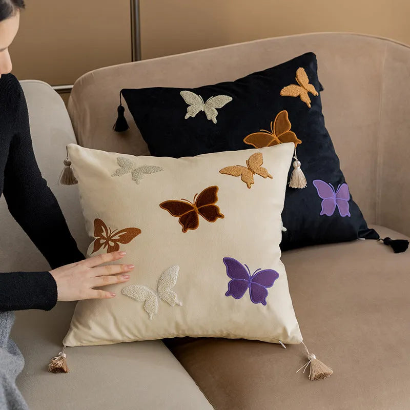 Square beige cushion with butterfly embroidery on a sofa, showing purple and black colour options.
